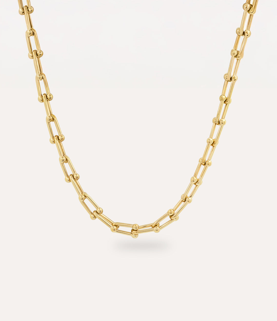Gold beaded-link chain necklace featuring U-shaped interconnected links on a cream background