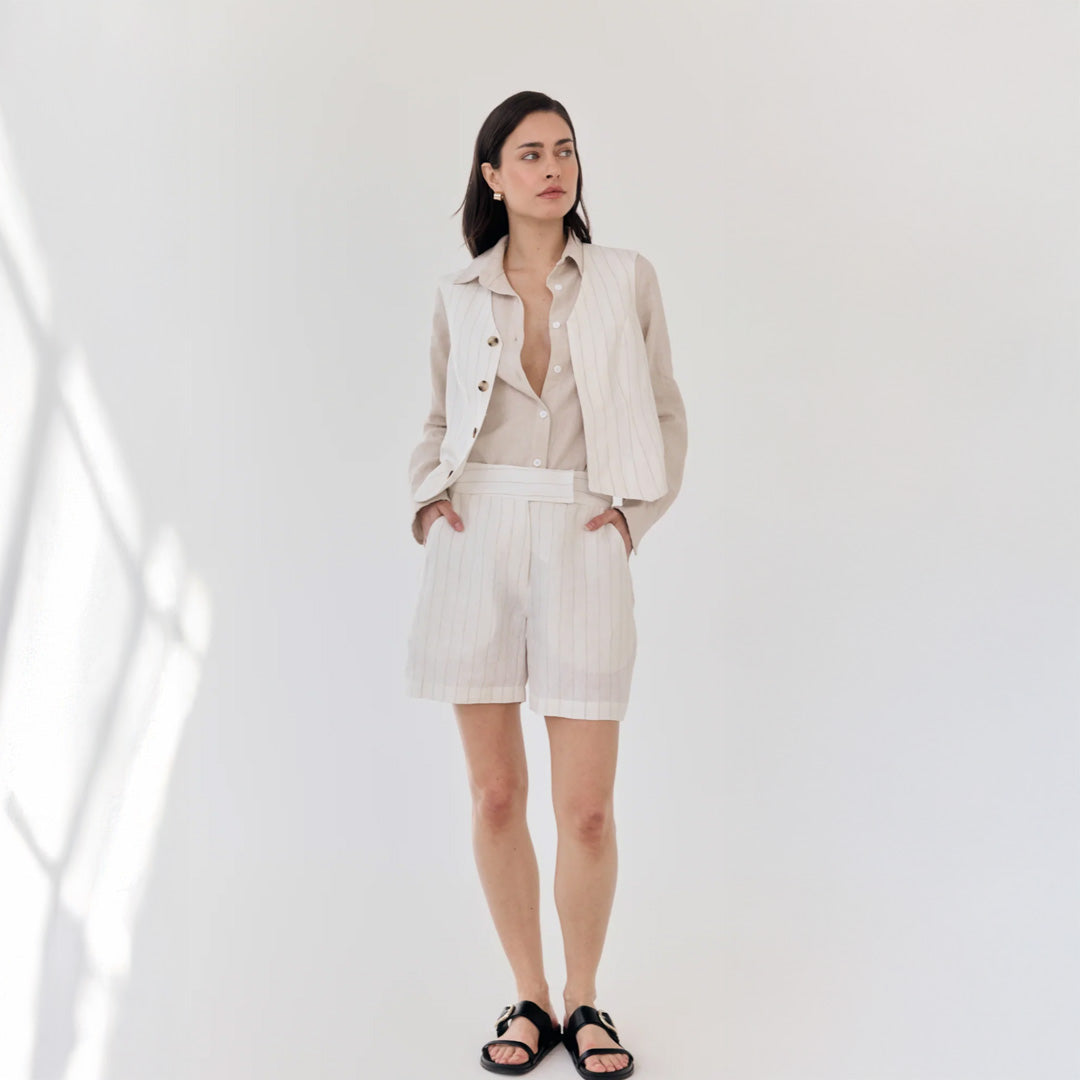 Woman wearing a light-colored outfit with a jacket and shorts on a white background