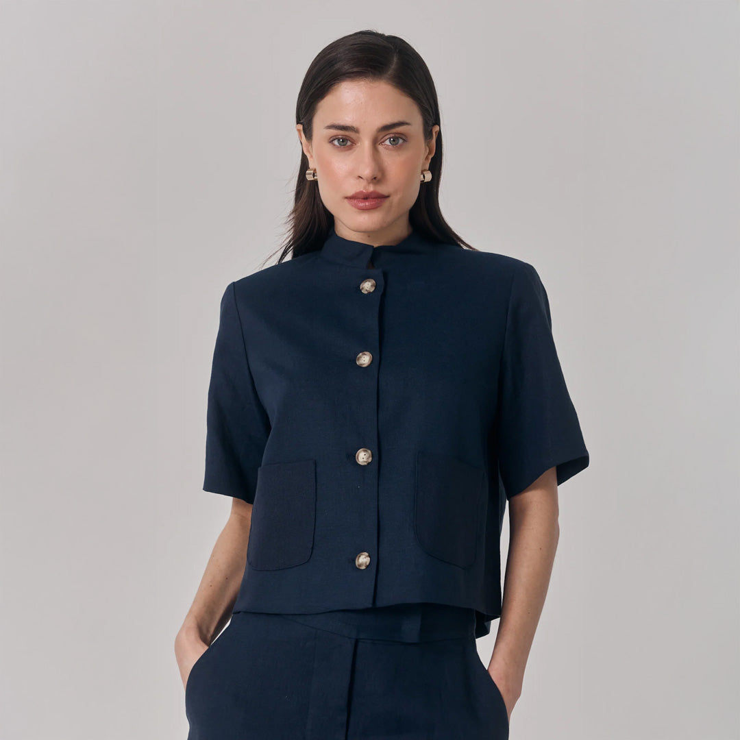Woman wearing a navy blue short-sleeve jacket with button details on a gray background