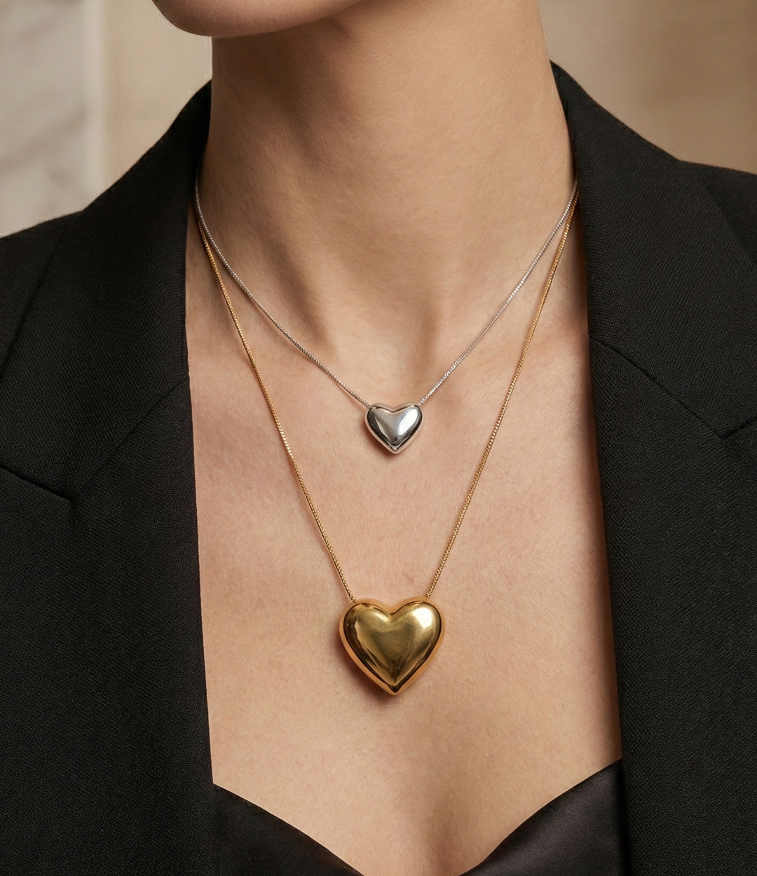 Two heart-shaped pendants on necklaces against a neutral background