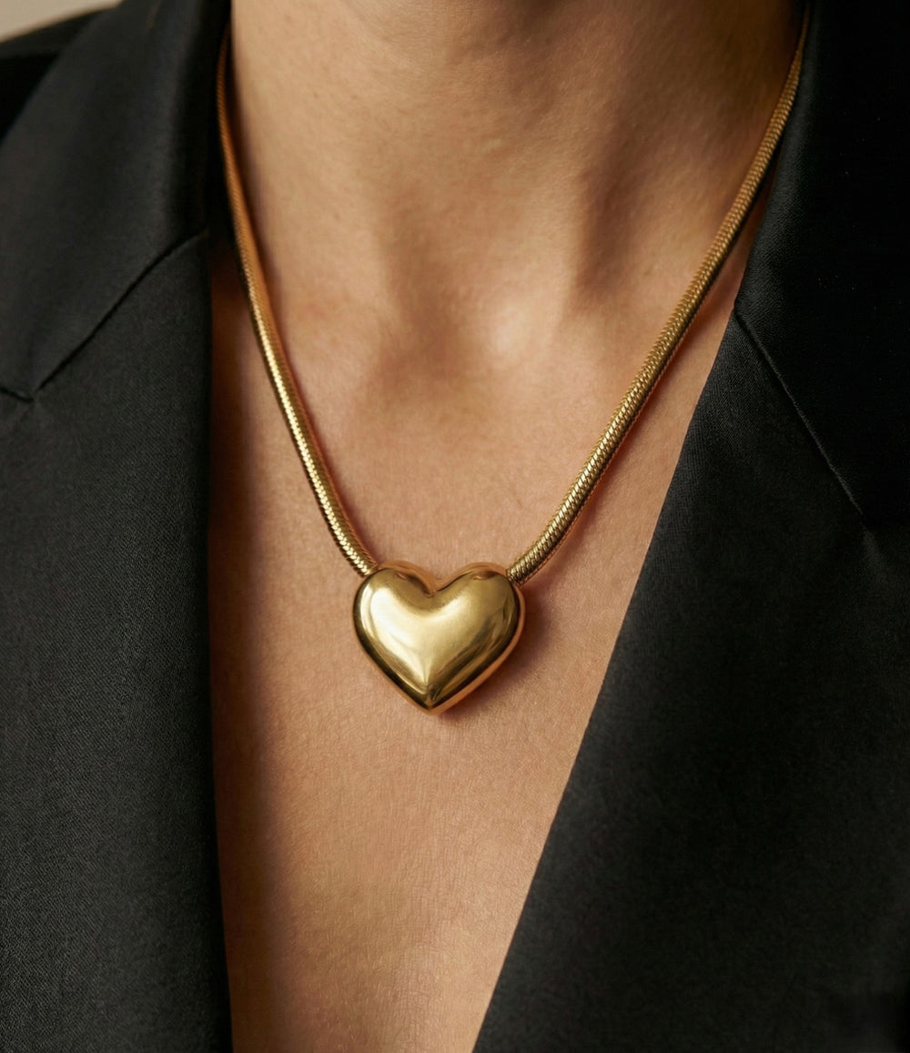 Gold heart-shaped necklace worn by a person against a black background