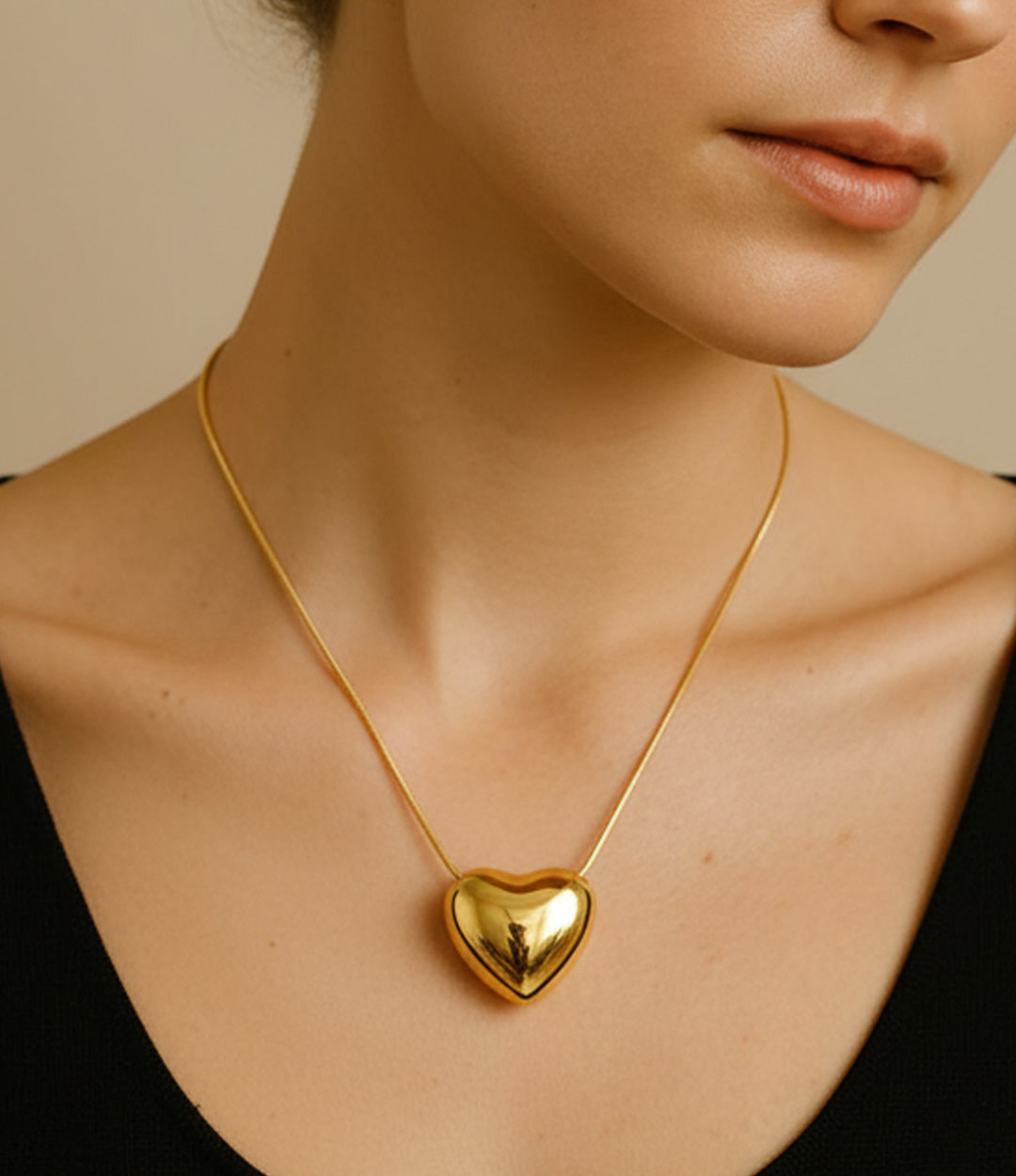 Gold heart-shaped necklace worn by a person against a neutral background