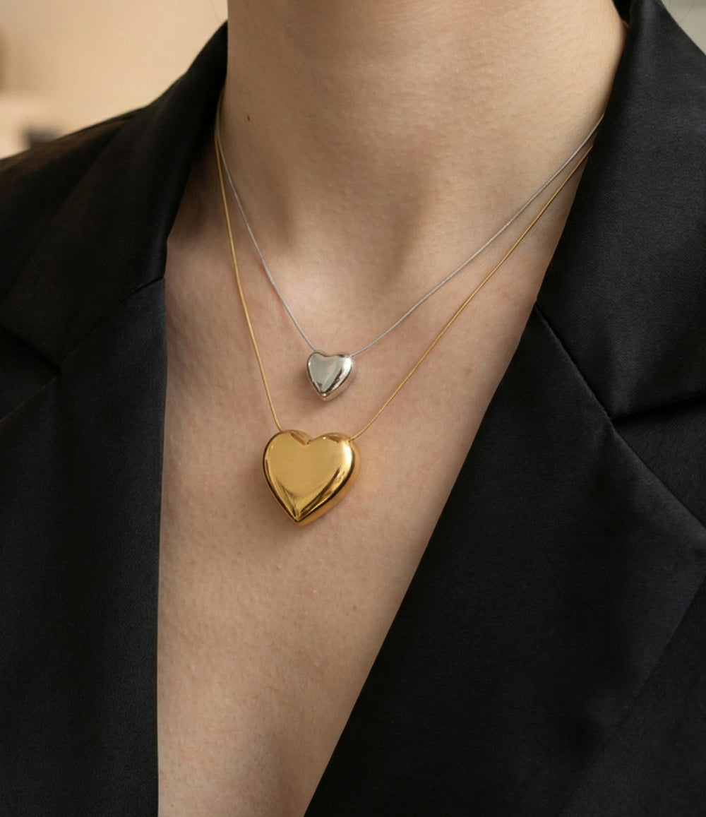 Two heart-shaped pendants on necklaces against a neutral background