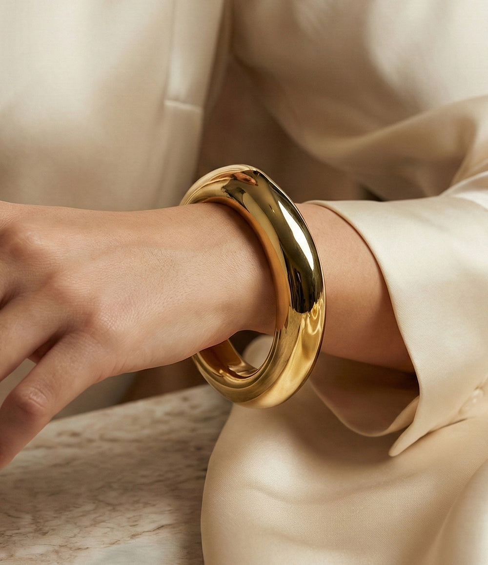 Gold bracelet on a wrist with a neutral background