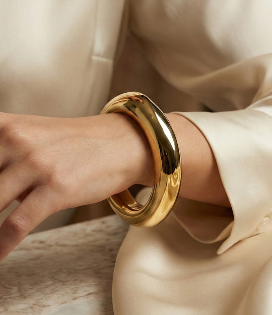 Gold bracelet on a wrist with a neutral background