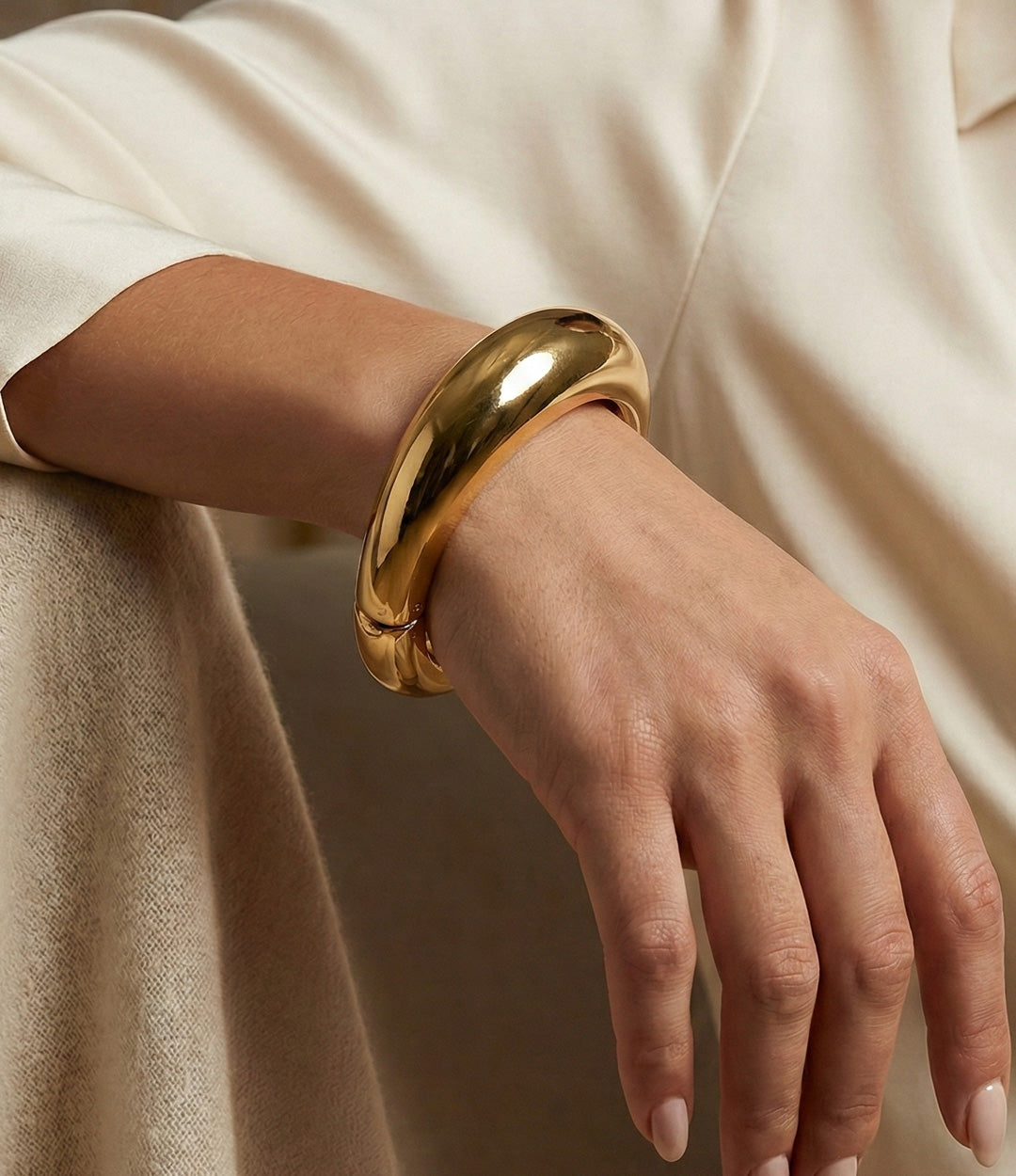 Gold bracelet on a wrist with a neutral background