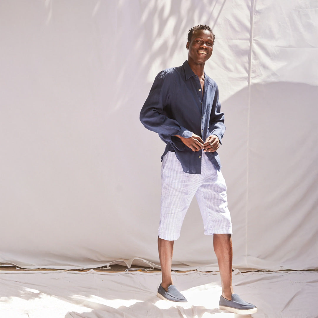 Man wearing a navy shirt and white shorts standing against a plain background