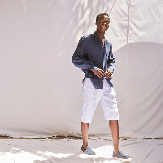 Man wearing a navy shirt and white shorts standing against a plain background