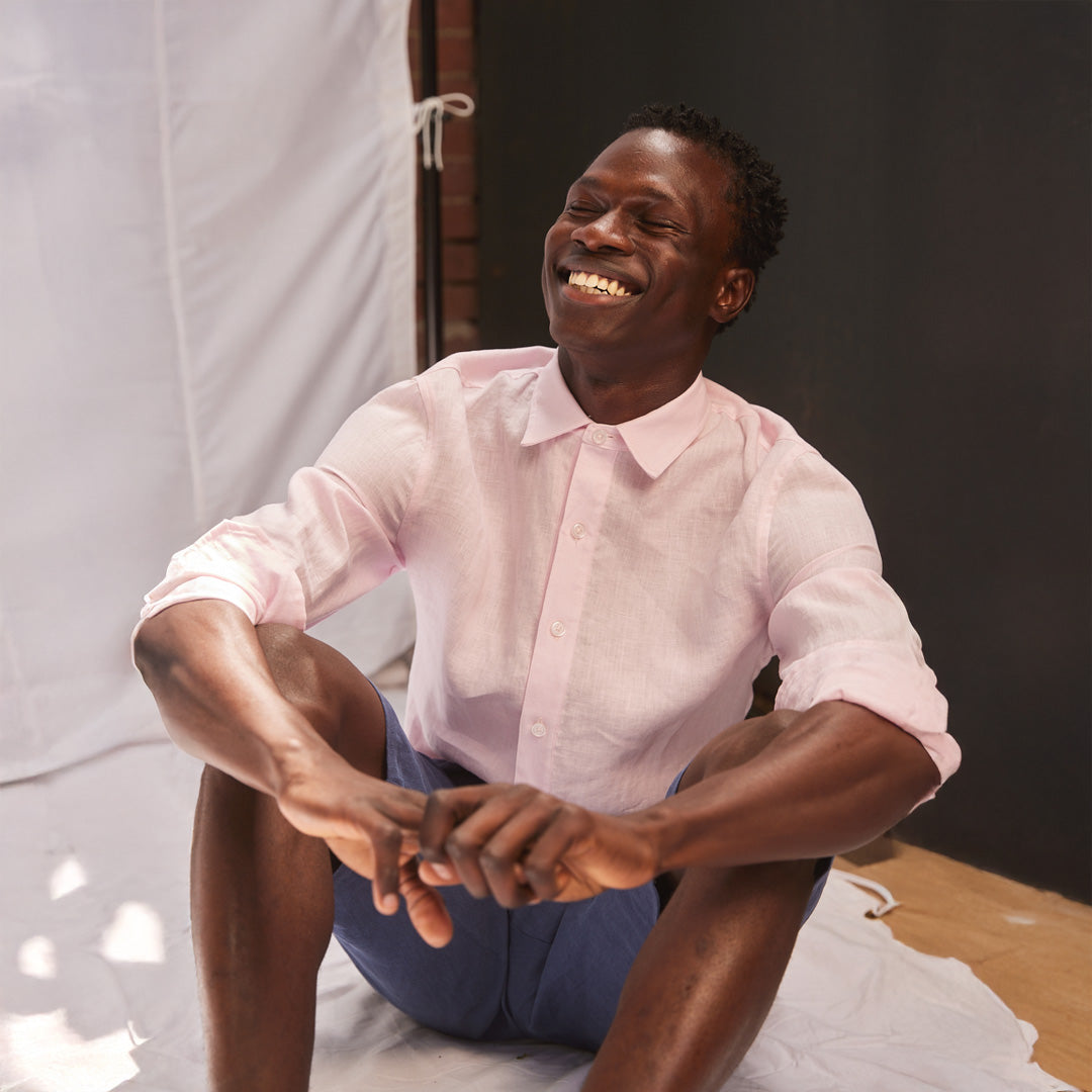 Man in a pink shirt sitting on a white surface with a dark background