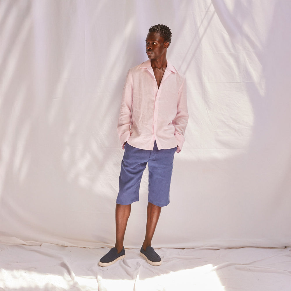 Man wearing a pink shirt and blue shorts standing against a white backdrop