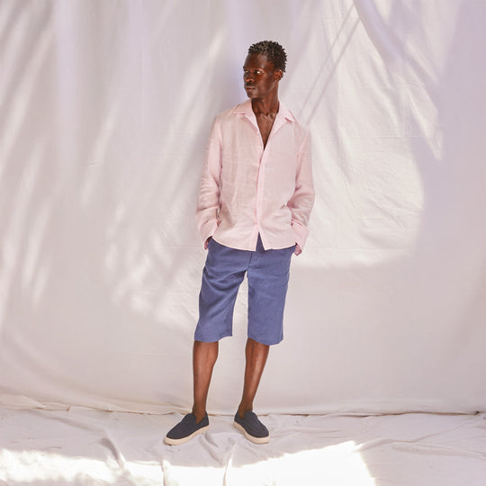 Man wearing a pink shirt and blue shorts standing against a white backdrop