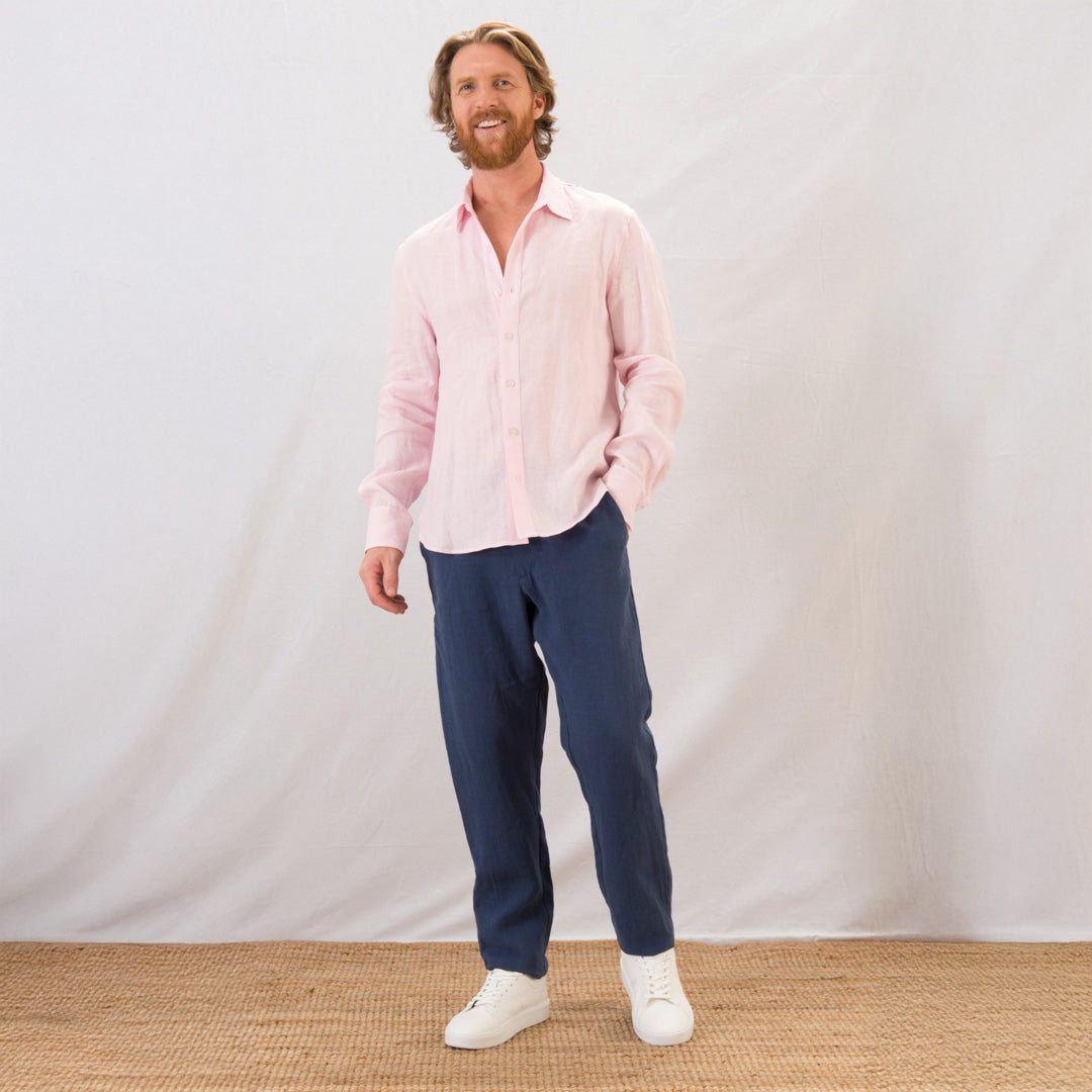 Man wearing a pink shirt and navy pants standing against a plain white background