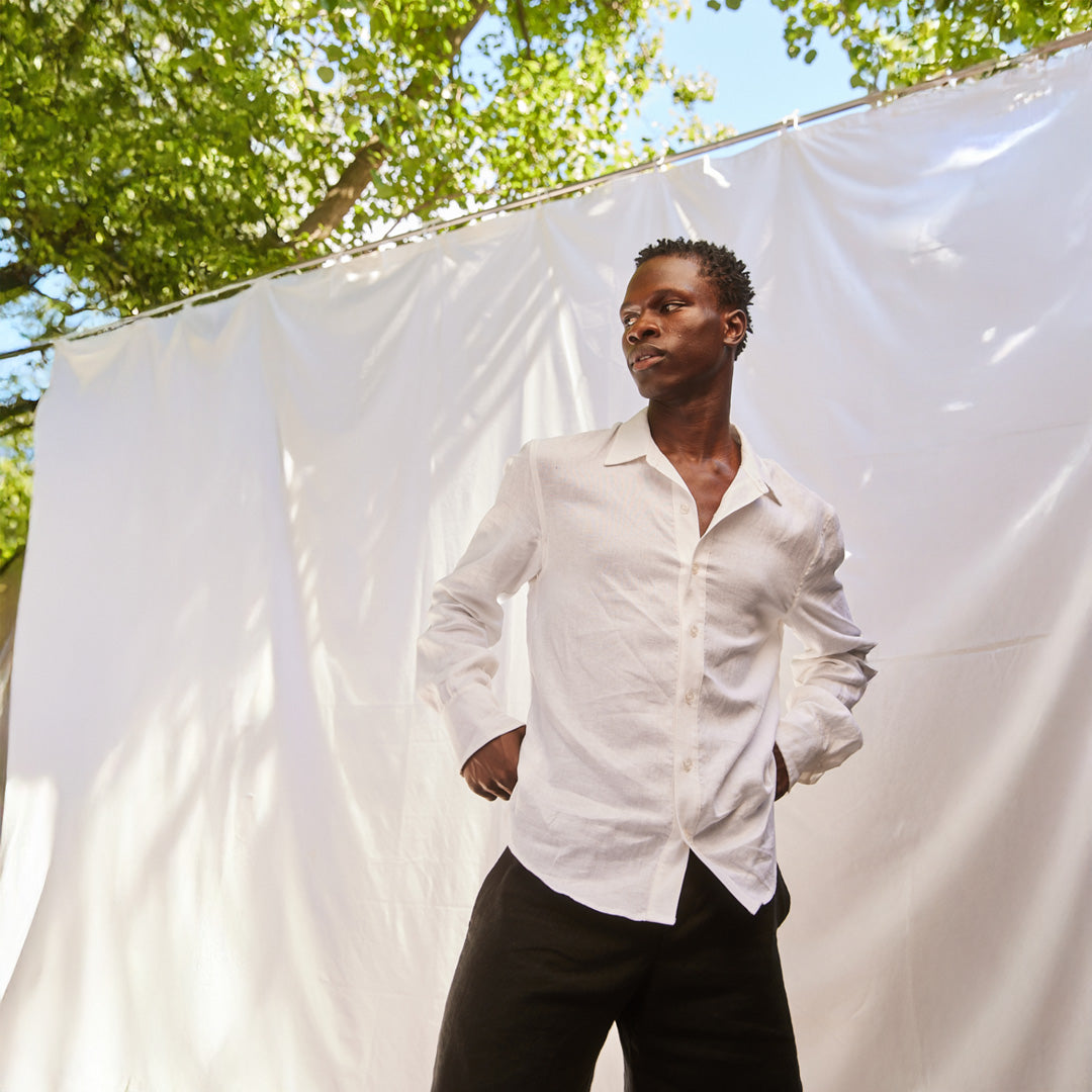 Man wearing a white shirt standing in front of a white sheet with trees in the background
