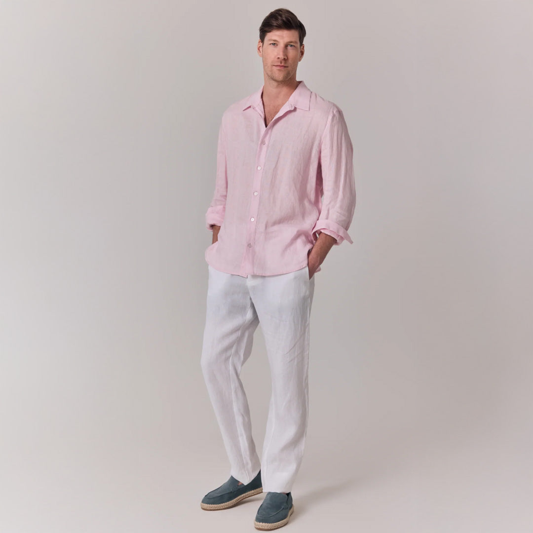 Man wearing a pink shirt and white pants against a plain background