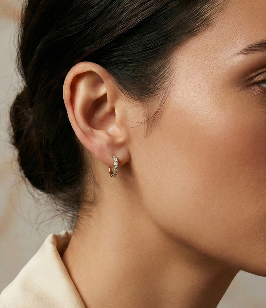 Close-up of a person wearing a small hoop earring with a neutral background