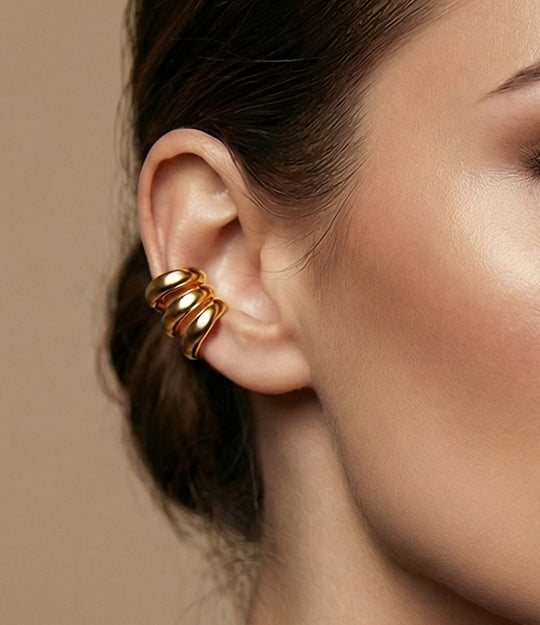 Close-up of a woman's ear wearing a gold earring against a neutral background