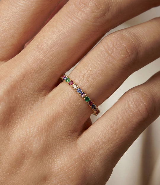 Woman's hand modeling the Mini Eternity Ring on the middle finger, stacked with other bands to show the colorful crystal details and dainty fit.