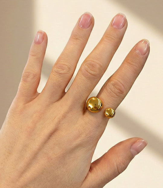 Model wearing the Mod Ball Ring in 18k gold plated finish, featuring a sleek open band with two gold spheres, isolated on a white background