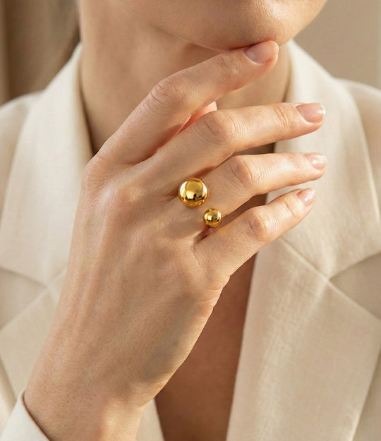 Close-up of a hand wearing two gold rings on a neutral background
