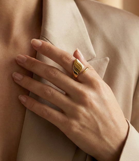 Hand wearing a gold ring with a neutral background