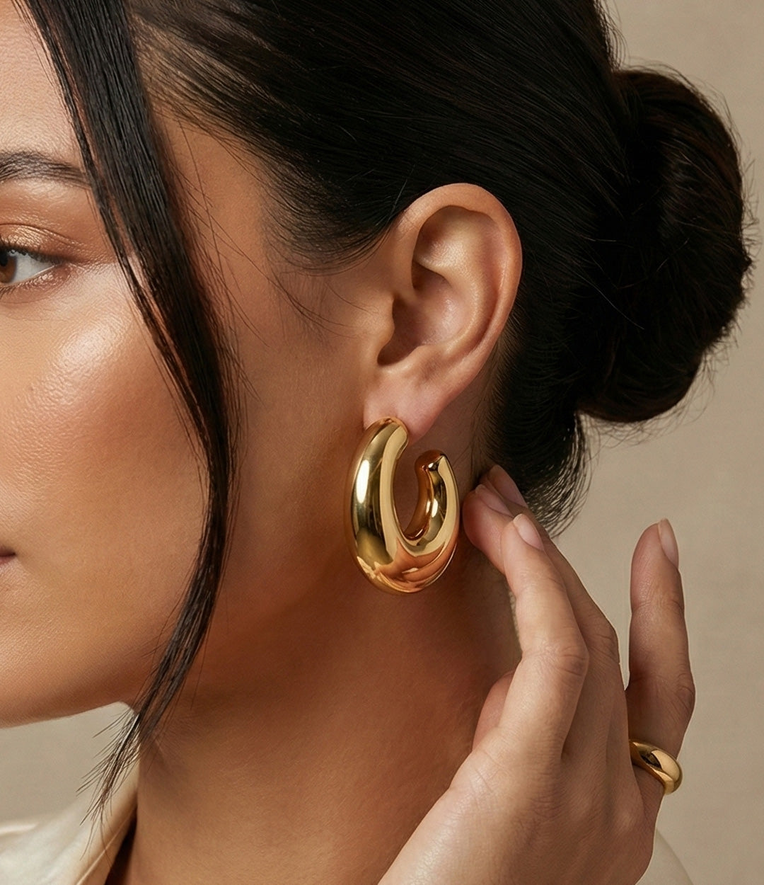 Close-up of a woman wearing gold hoop earrings with a neutral background