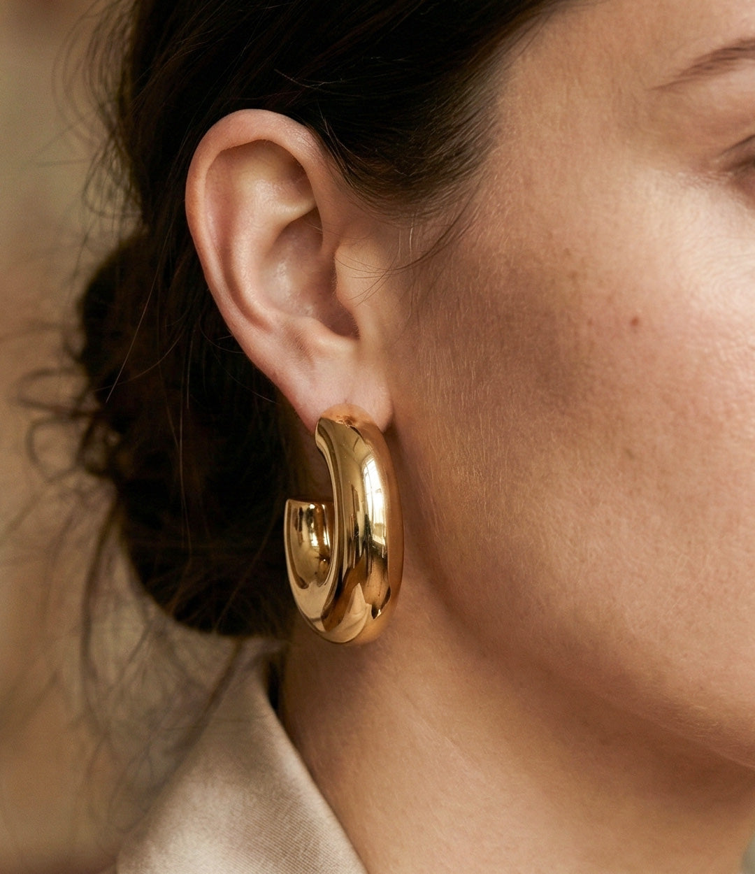 Close-up of a woman wearing gold hoop earrings with a neutral background