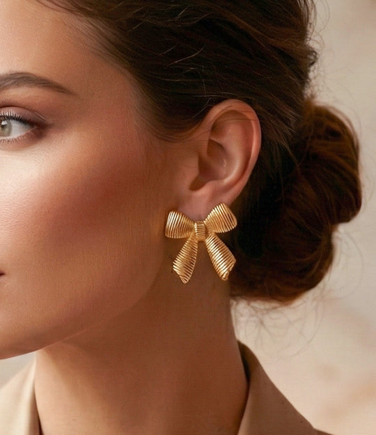Gold bow-shaped earrings worn by a model with a neutral background