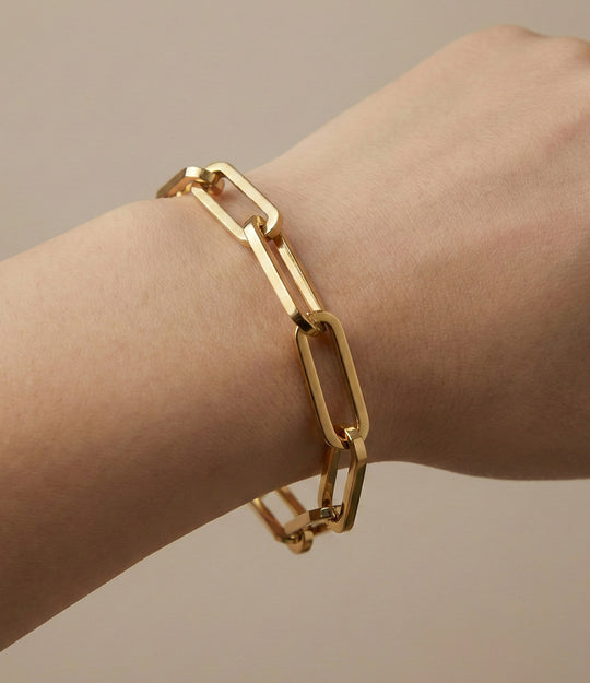 Gold chain bracelet on a wrist against a neutral background