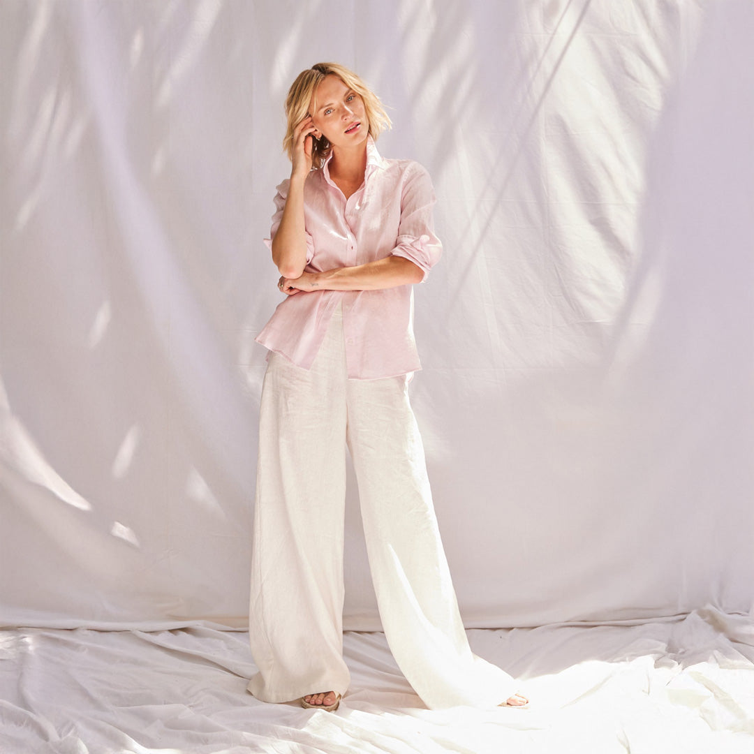 Person wearing a light pink shirt and white pants against a white background