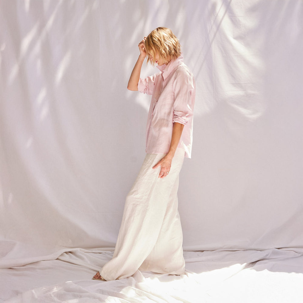 Person wearing a light pink shirt and white pants standing against a plain white background