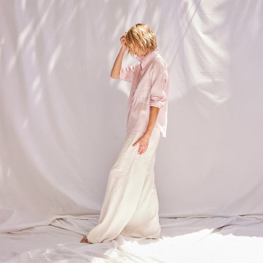 Person wearing a light pink shirt and white pants standing against a plain white background