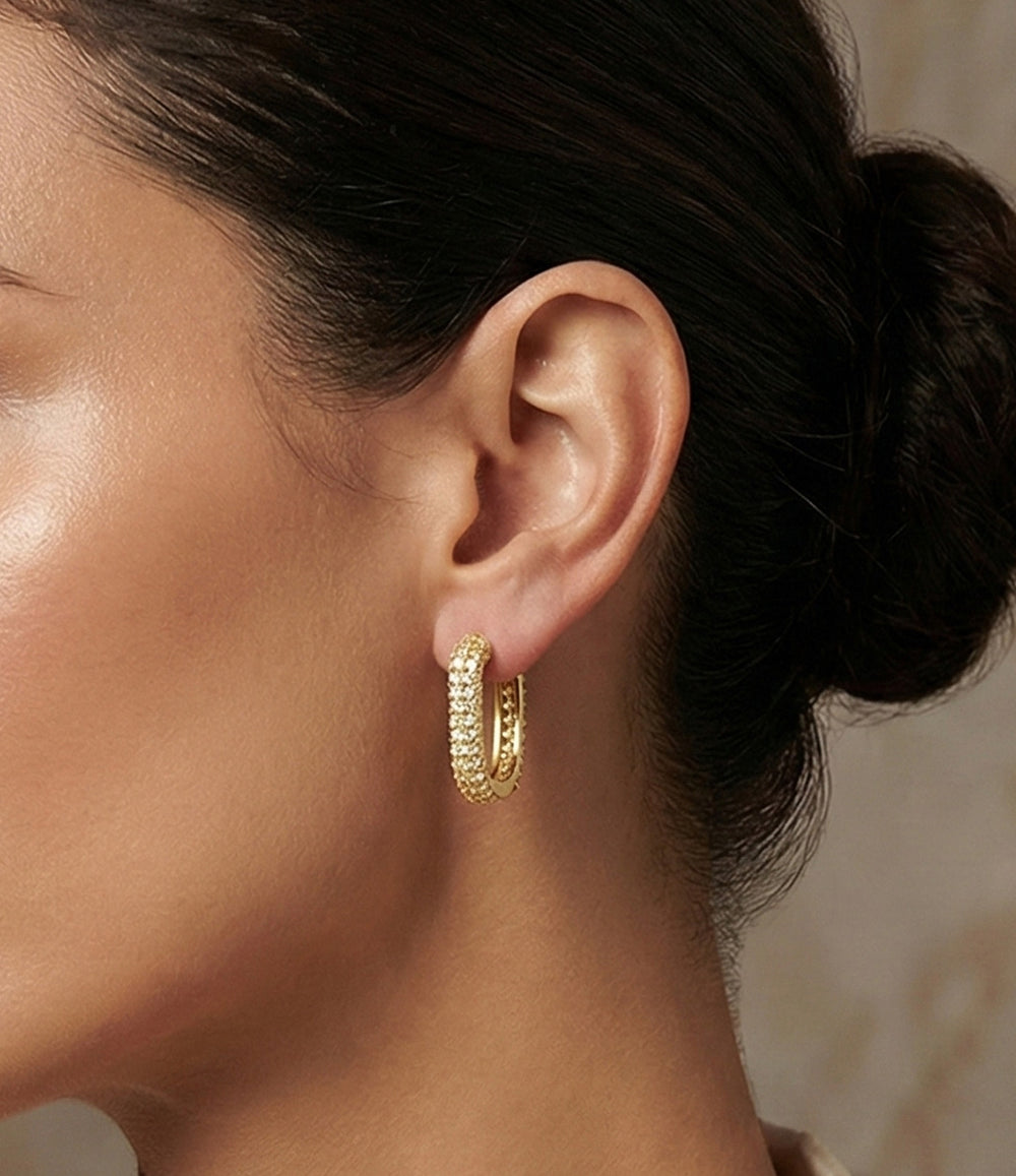 Close-up of a person wearing gold hoop earrings with a blurred background