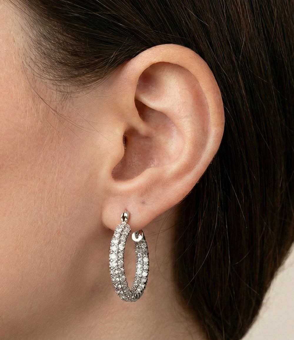 Close-up of an ear wearing a silver hoop earring with clear stones.