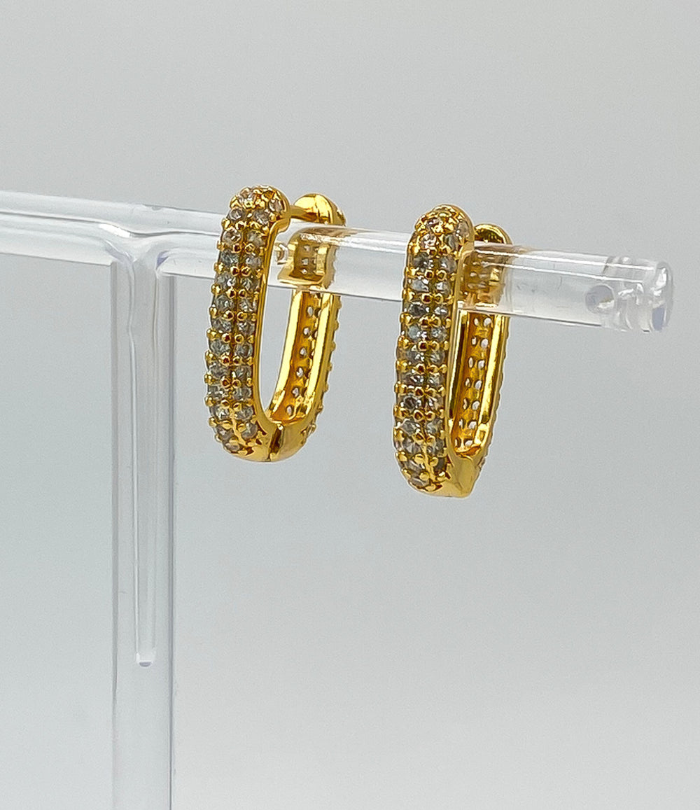 Gold hoop earrings with embedded stones on a clear stand against a gray background