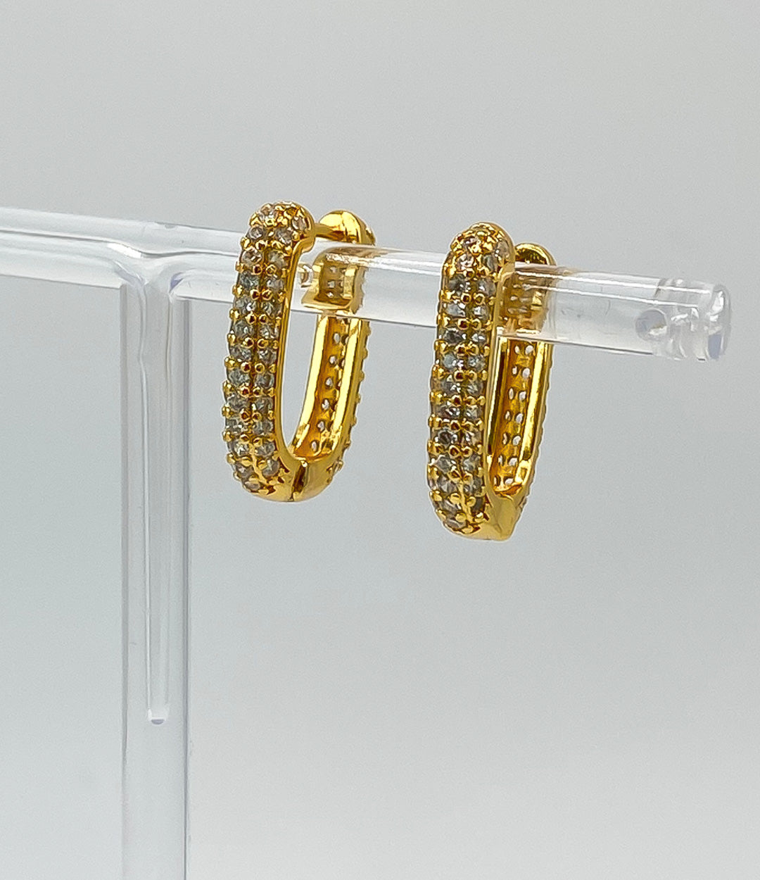 Gold hoop earrings with embedded stones on a clear stand against a gray background