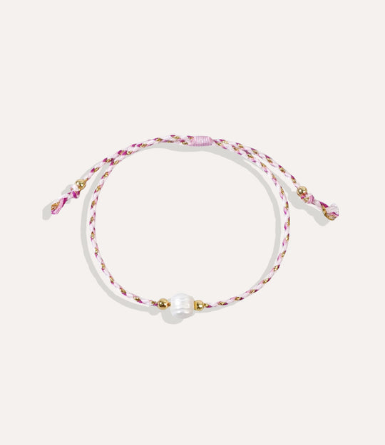 Pearl on a pink string bracelet displayed on a neutral background showcasing its vibrant cord and glossy pearl.