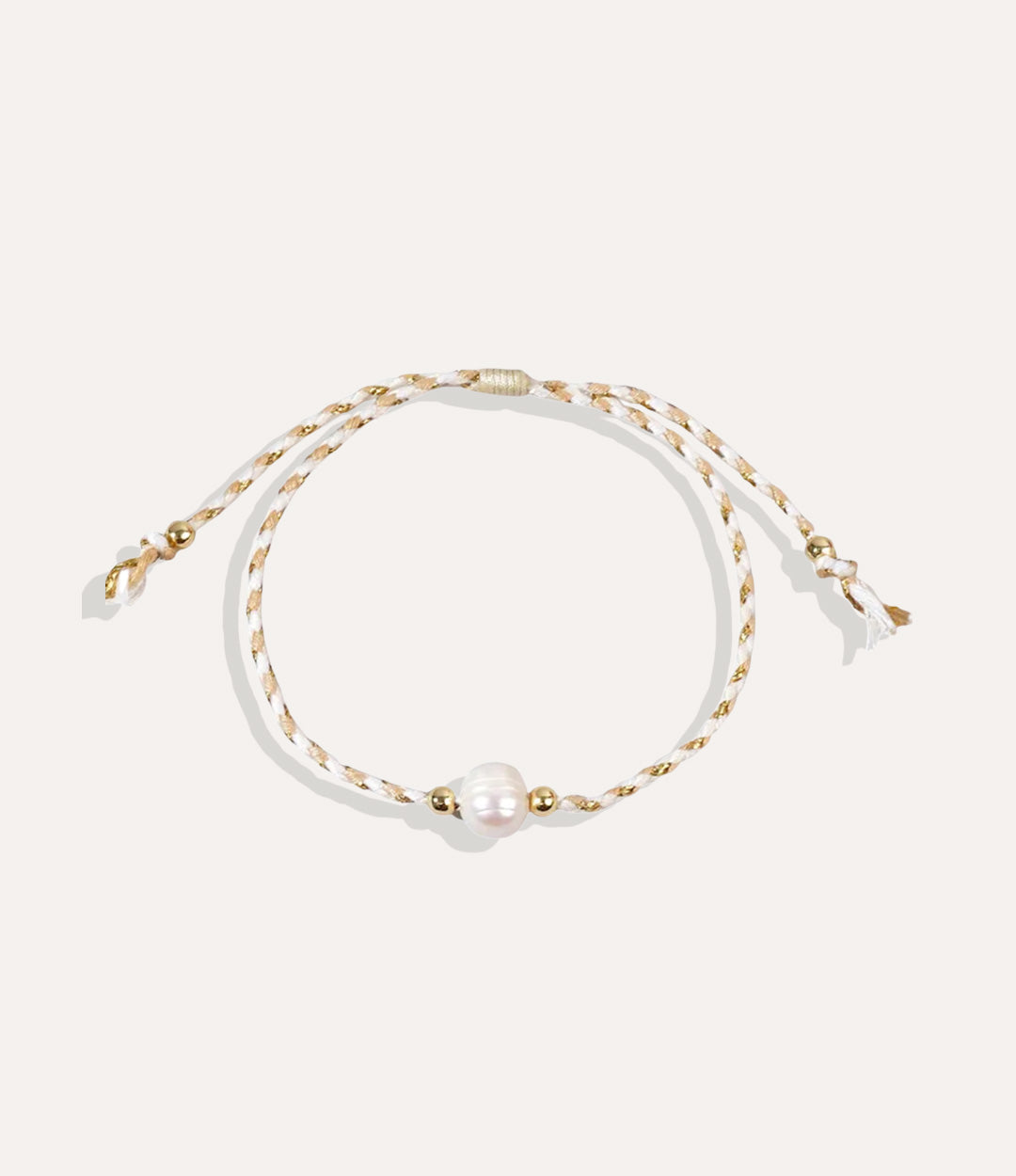 Pearl on a white and tan string bracelet displayed on a neutral background showcasing its vibrant cord and glossy pearl.
