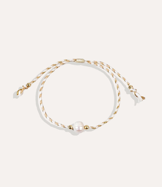 Pearl on a white and tan string bracelet displayed on a neutral background showcasing its vibrant cord and glossy pearl.