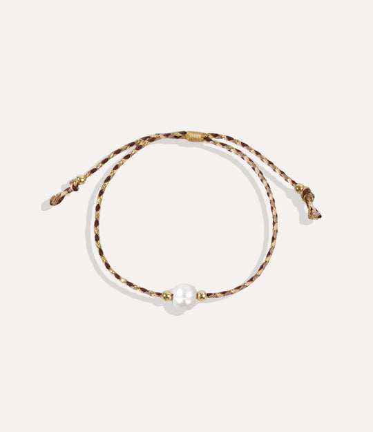 Pearl on a brown string bracelet displayed on a neutral background showcasing its vibrant cord and glossy pearl.
