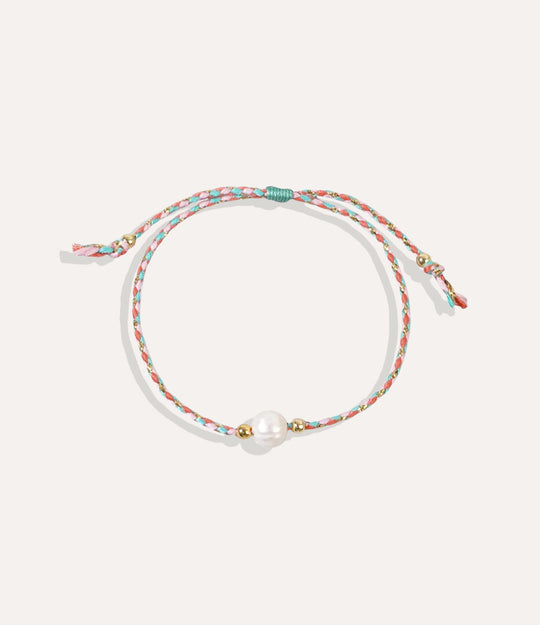 Pearl on a coral turquoise string bracelet displayed on a neutral background showcasing its vibrant cord and glossy pearl.