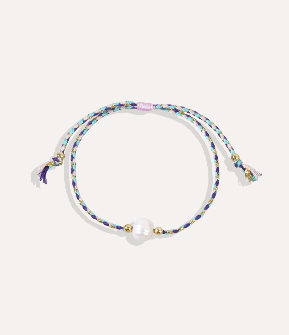 Pearl on a purple string bracelet displayed on a neutral background showcasing its vibrant cord and glossy pearl.