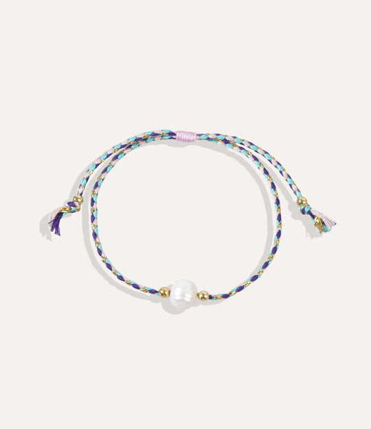 Pearl on a purple string bracelet displayed on a neutral background showcasing its vibrant cord and glossy pearl.