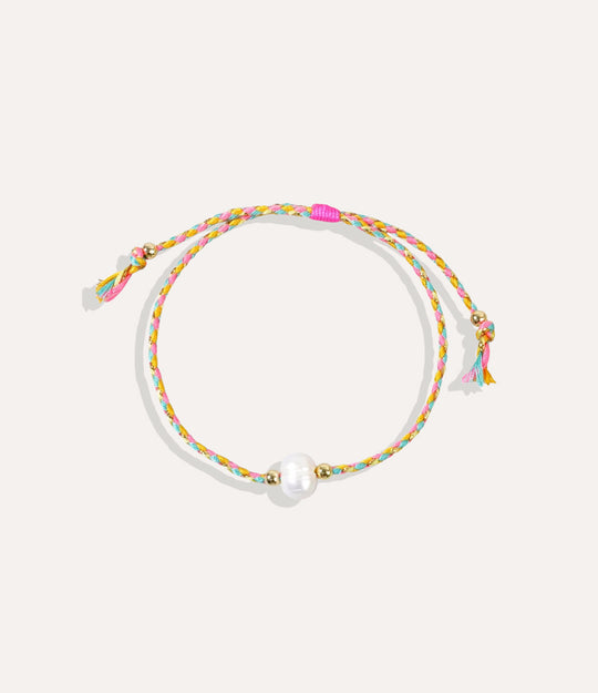 Pearl on a yellow and pink string bracelet displayed on a neutral background showcasing its vibrant cord and glossy pearl.