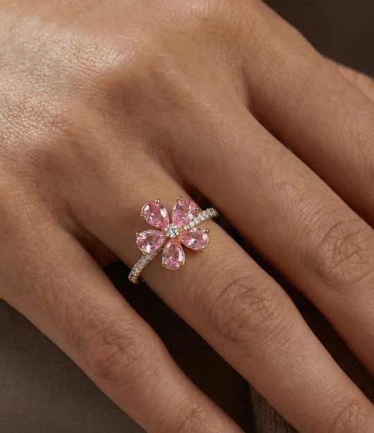 Woman's hand wearing the Pink Flower Ring on the ring finger, showcasing the sparkling diamond details and elegant floral design against a neutral background.