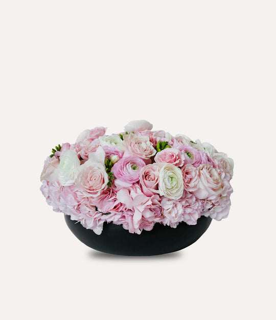 Bouquet of pink and white flowers in a black bowl on a light gray background