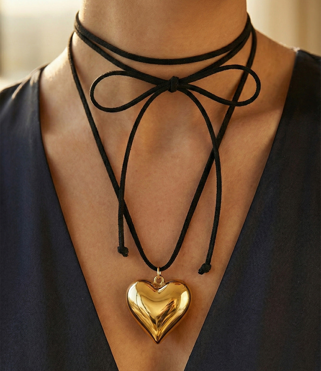 Black choker necklace with a gold heart pendant on a person wearing a dark blue top.
