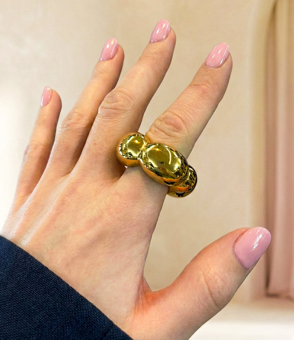 Hand wearing a large gold ring against a neutral background