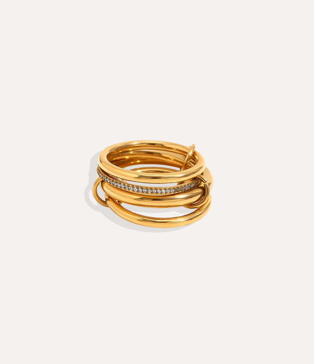 Stack of gold rings with embedded stones on a light beige background