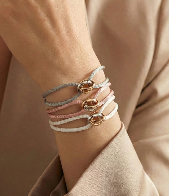 Close-up of a wrist wearing multiple bracelets with gold rings on a neutral background
