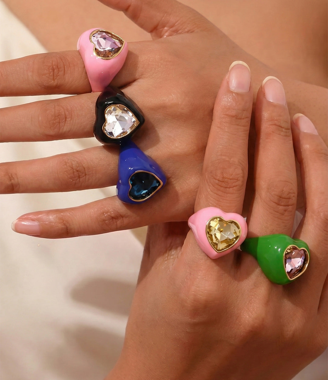 Hand wearing colorful heart-shaped rings with gemstones on a neutral background